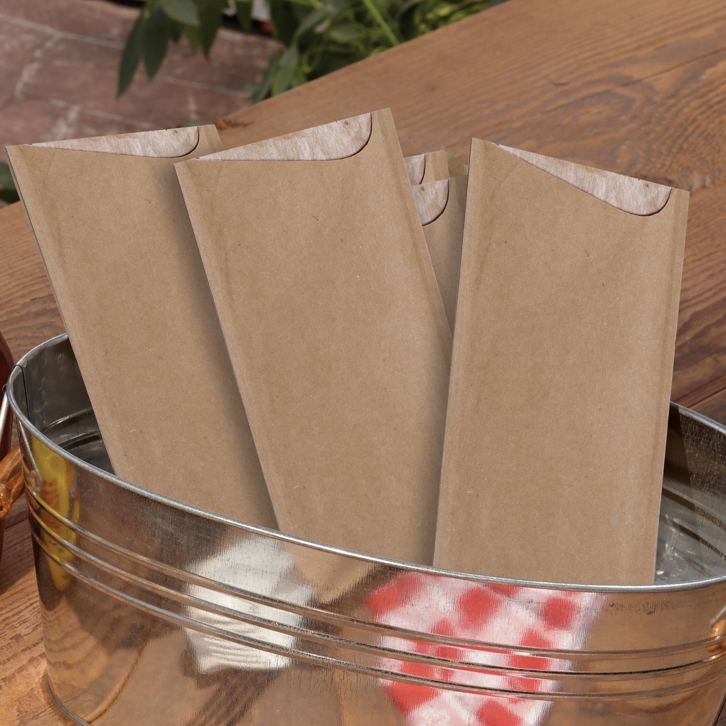 Brown paper cutlery pouches in a metal bucket on a wooden surface