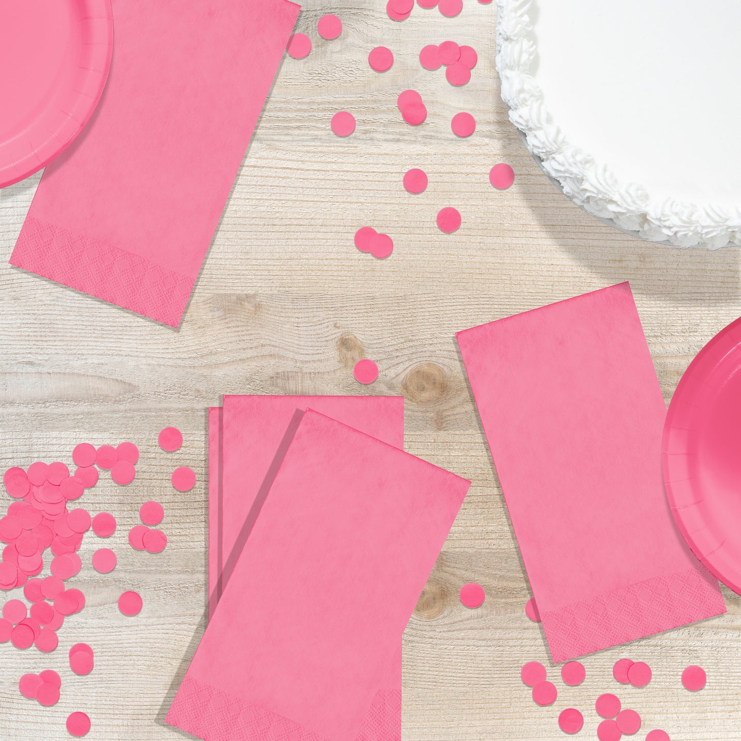 Pink party supplies including napkins and confetti on a wooden surface