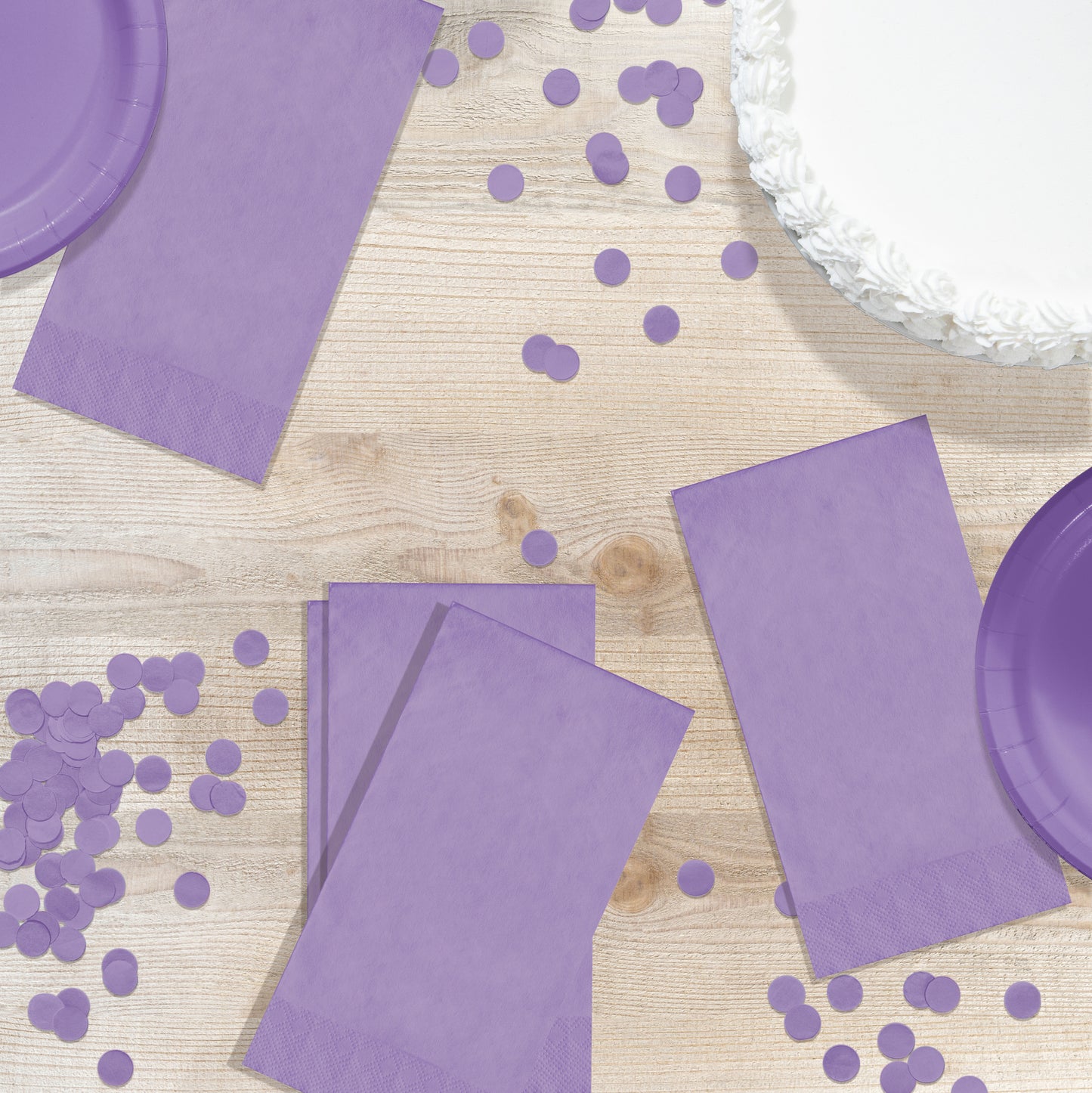 Purple party supplies including napkins and plates on a wooden surface with scattered purple confetti.