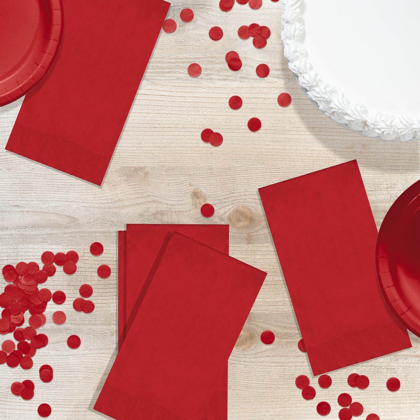 Red pin embossed guest napkins on a wood table with red circle confetti
