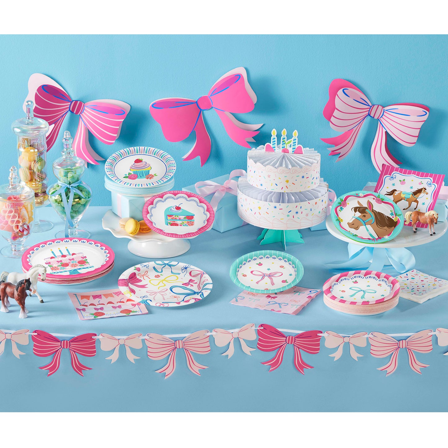 Birthday party setup with cake, plates, and decorations on a blue tablecloth against a blue wall