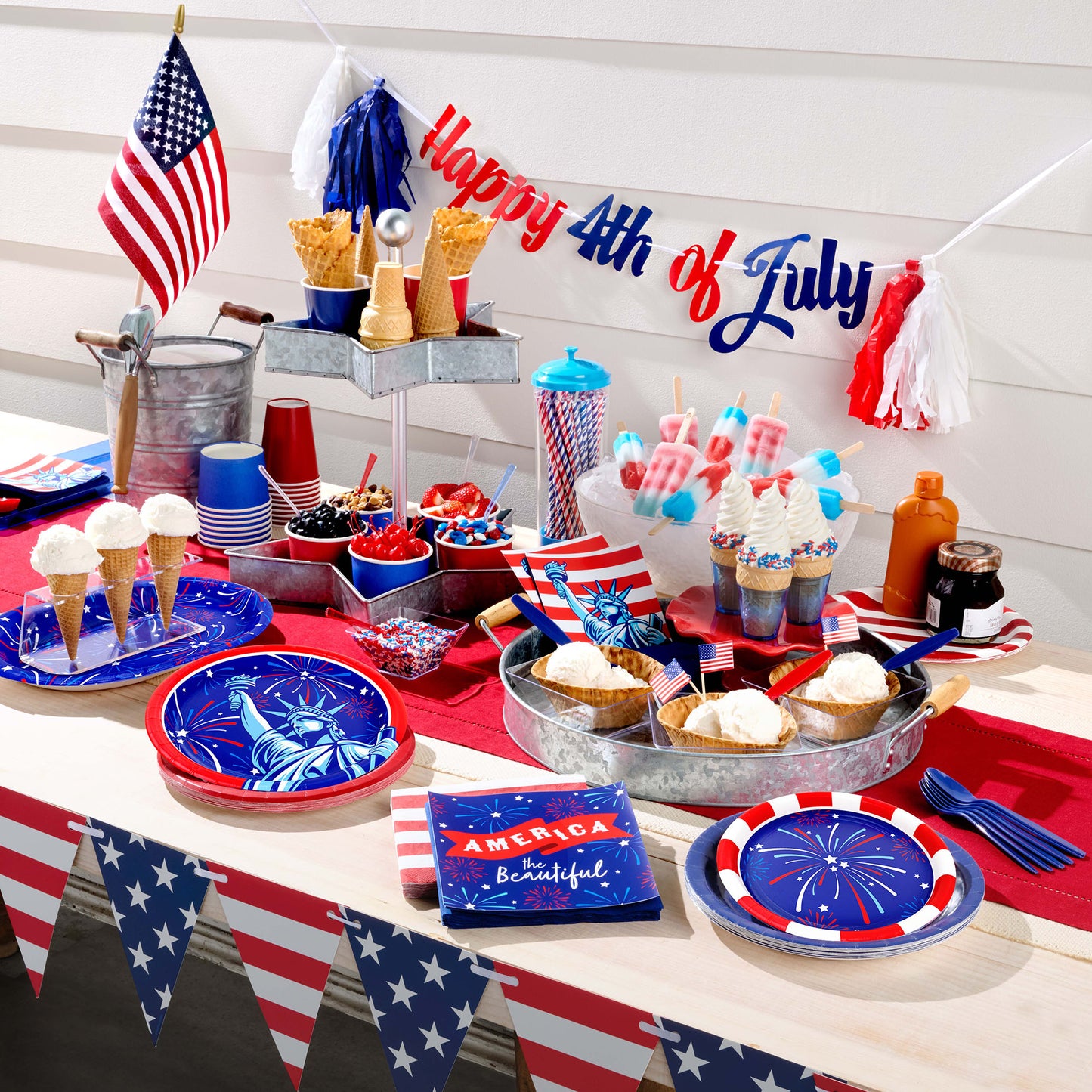Table setting for 4th of July celebration with decorations, food, and a 'Happy 4th of July' banner.