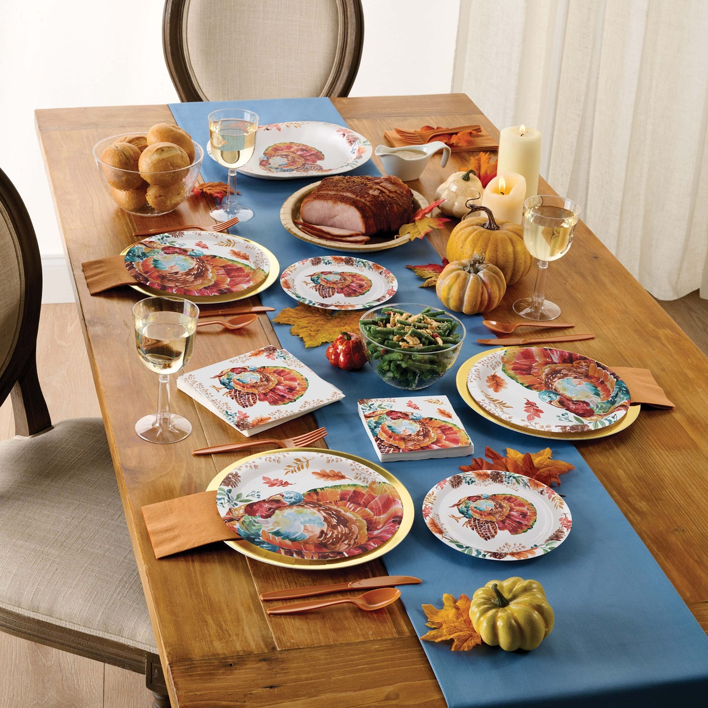 Tasteful Turkey Oval Dinner Paper Plates 96 ct displayed on a a wooden table with autumn decorations and tableware