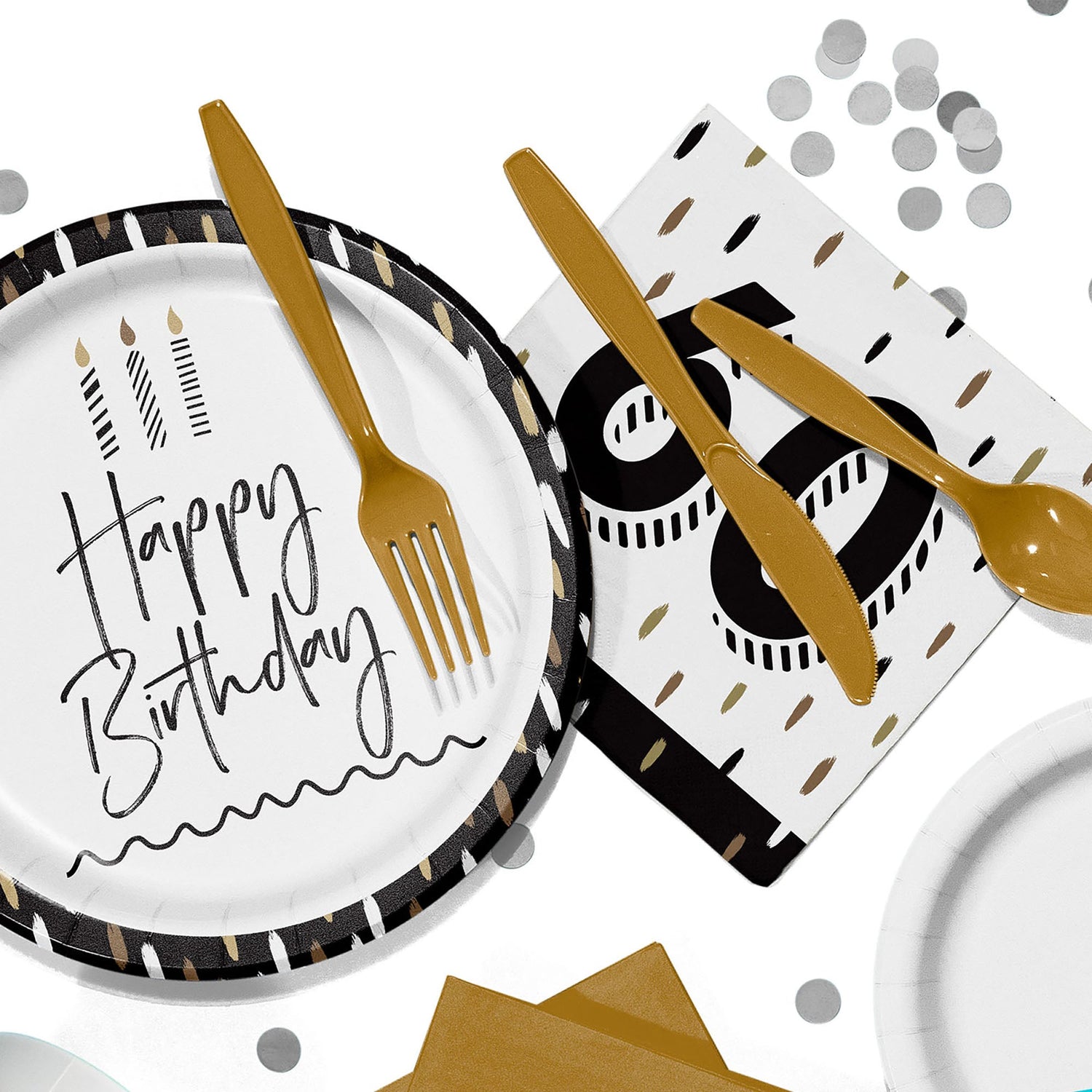Flat lay of black, white, and gold birthday party tableware, including a paper plate that reads “Happy Birthday,” gold plastic cutlery, a napkin with a large “60,” and scattered silver confetti on a white background.