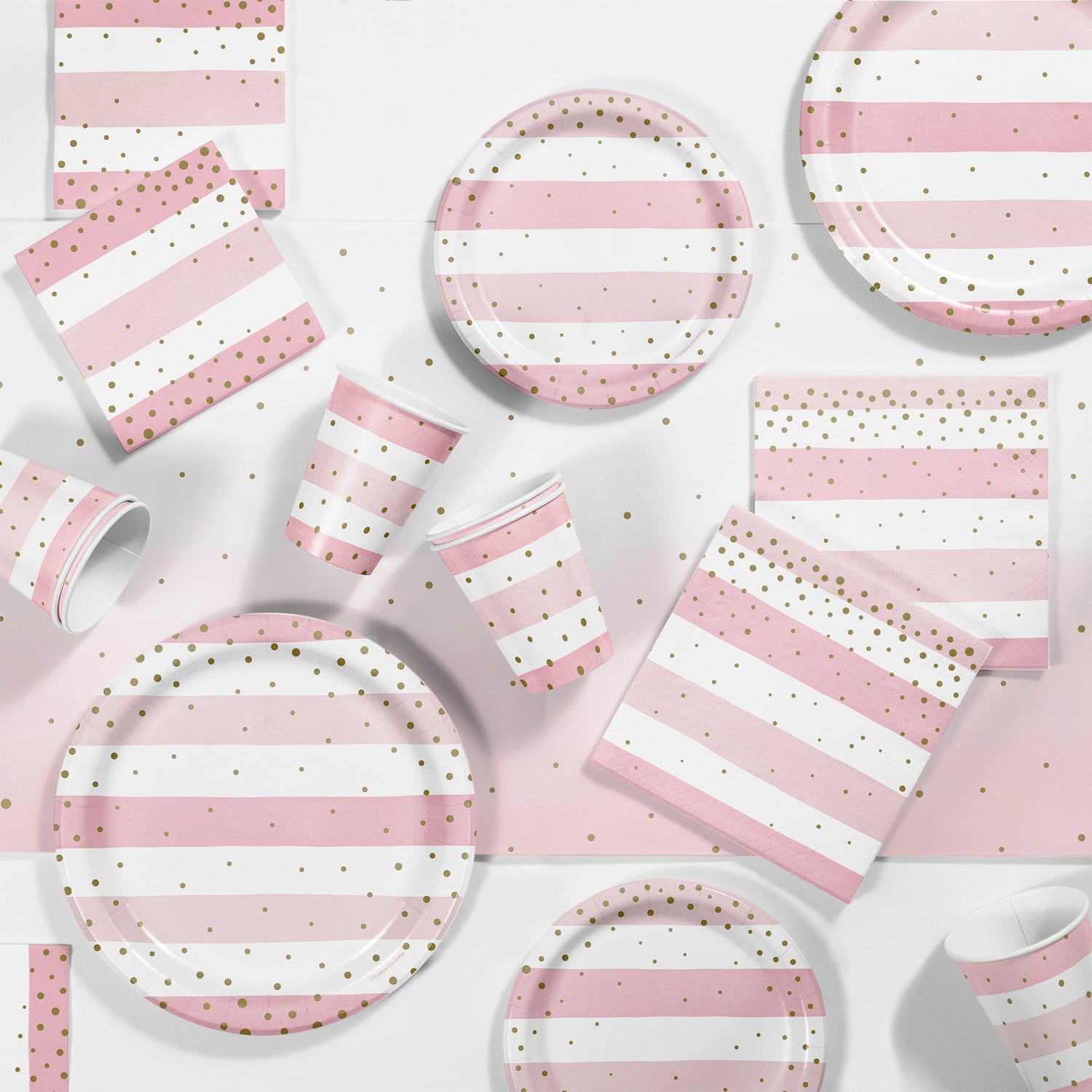 Pink and Gold Celebration Baby Shower Supplies. Pink and white striped plates, napkins and cups with gold polka dots displayed on a table