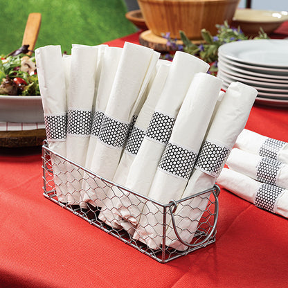 Rolled white napkins with black and white hexagon napkin band in a metal basket on a red tablecloth.