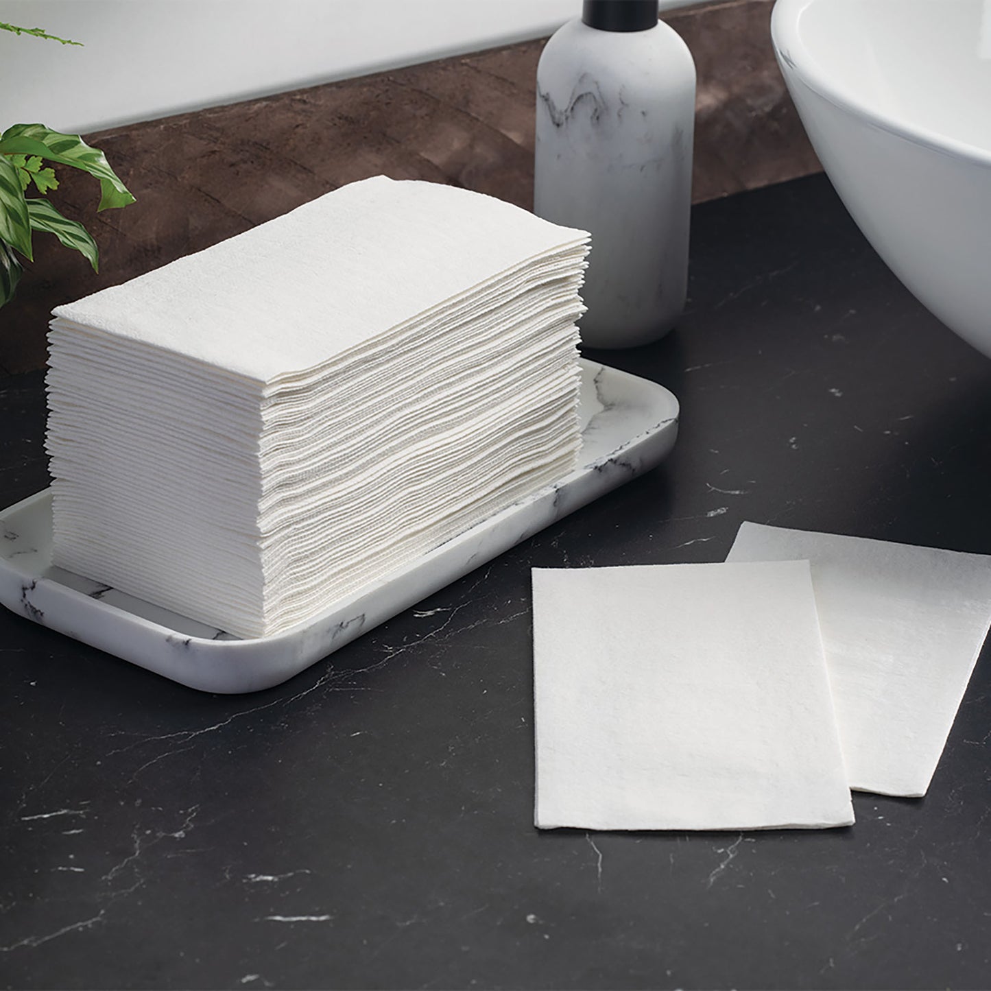 Stack of white napkins on a marble tray with a marble bottle and sink in the background.