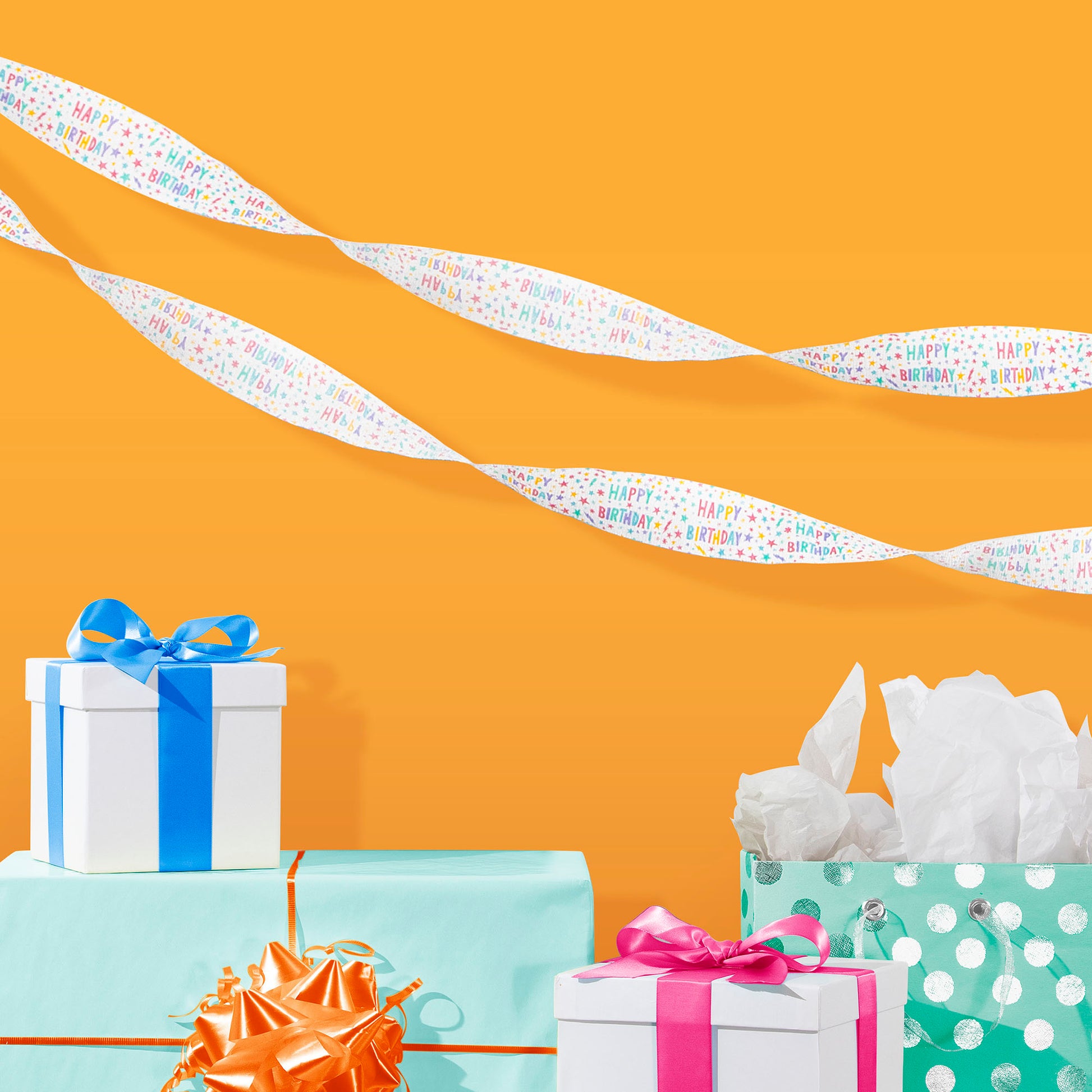 White crepe streamer with multicolored "Happy Birthday" and stars on an orange background and birthday presents
