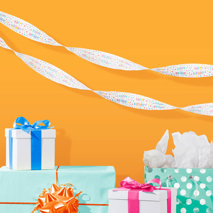 White crepe streamer with multicolored "Happy Birthday" and stars on an orange background and birthday presents