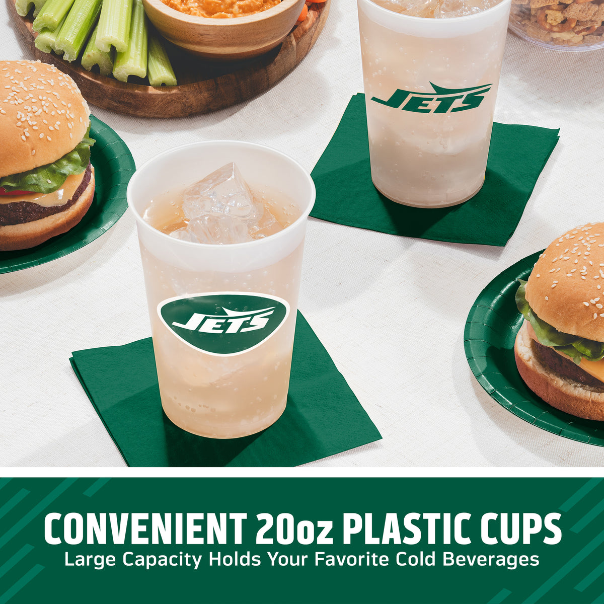 Three clear 20oz plastic cups with green Jets logos are shown on dark green napkin on a table, each filled with a light-colored beverage. Hamburgers on green paper plates and celery in a bowl are visible in the background.