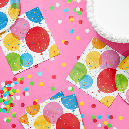 Colorful party napkins with balloons on a pink surface with confetti.