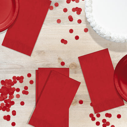Red paper plates and napkins with scattered red confetti on a wooden surface