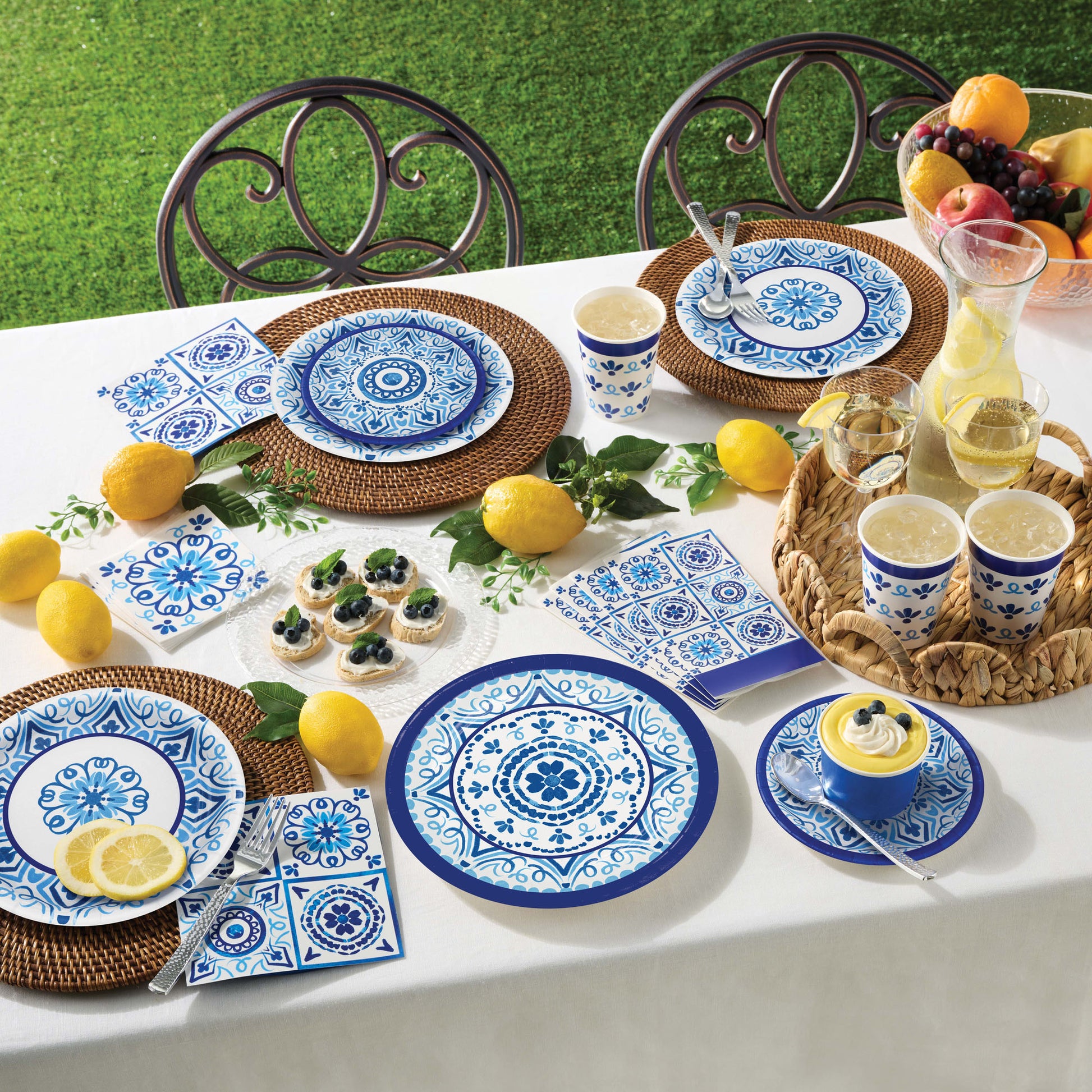 Outdoor table setting with blue and white paper plates, cups, and napkins on a white tablecloth.