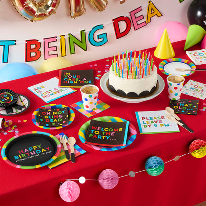 Birthday party setup with cake, plates, and decorations on a red tablecloth.