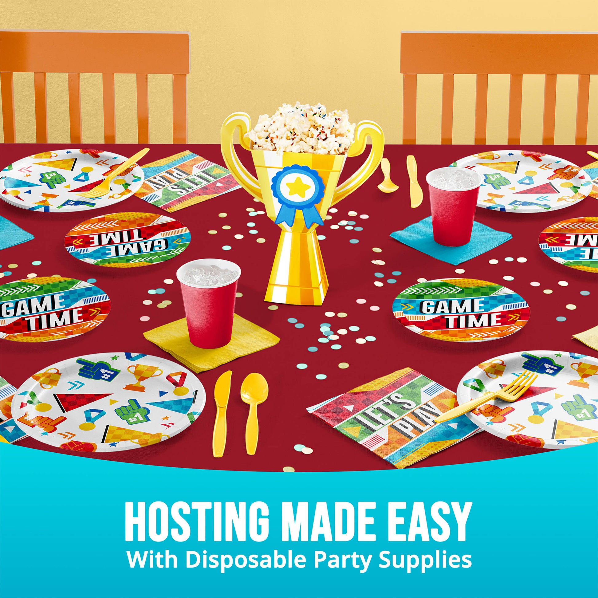 Disposable party supplies on a table with 'Game Time' plates, cups, and a trophy centerpiece.